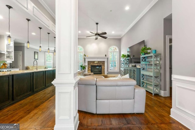 living area with crown molding, dark wood finished floors, a ceiling fan, and a stone fireplace