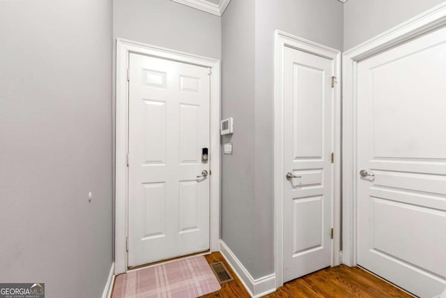 doorway with crown molding, dark wood finished floors, visible vents, and baseboards