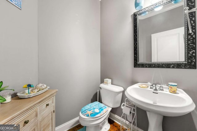 half bathroom with baseboards, toilet, and wood finished floors
