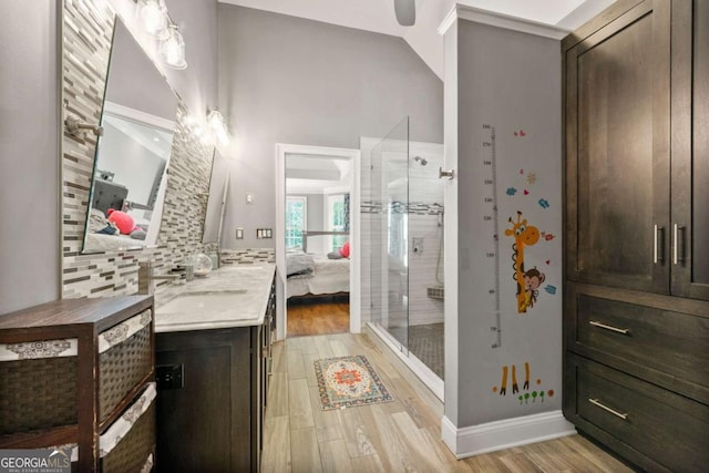ensuite bathroom featuring wood finished floors, vanity, a stall shower, decorative backsplash, and connected bathroom