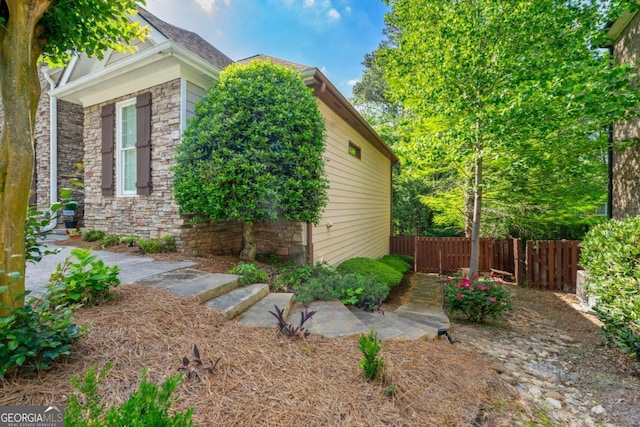 view of side of property with stone siding and fence