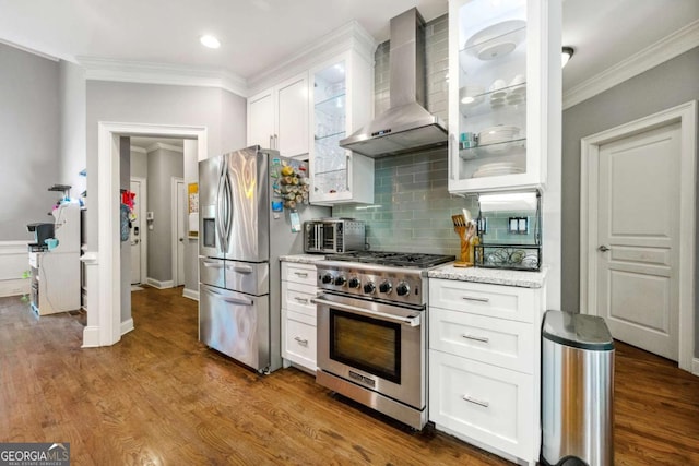kitchen with stainless steel appliances, ornamental molding, wall chimney exhaust hood, white cabinetry, and backsplash