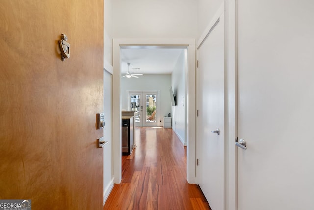 corridor with french doors, wood finished floors, and baseboards