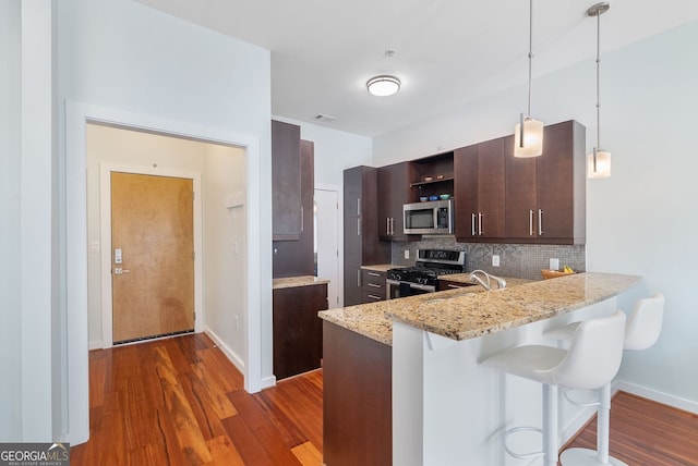 kitchen featuring dark brown cabinets, a kitchen bar, open shelves, backsplash, and appliances with stainless steel finishes
