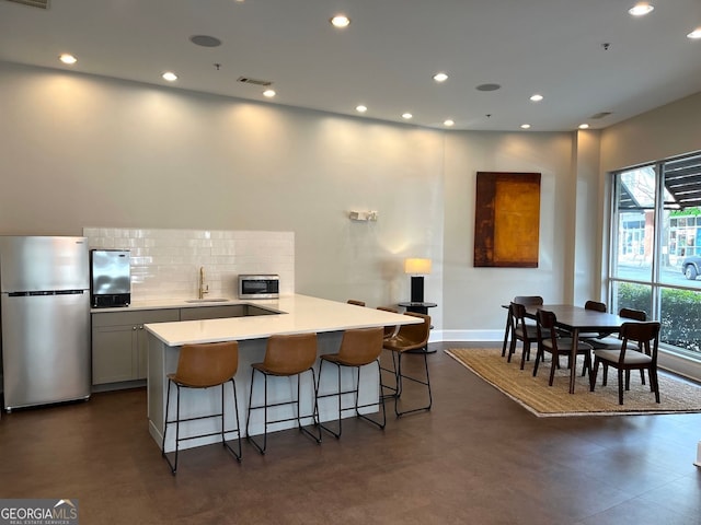 kitchen with a sink, a kitchen breakfast bar, decorative backsplash, light countertops, and appliances with stainless steel finishes