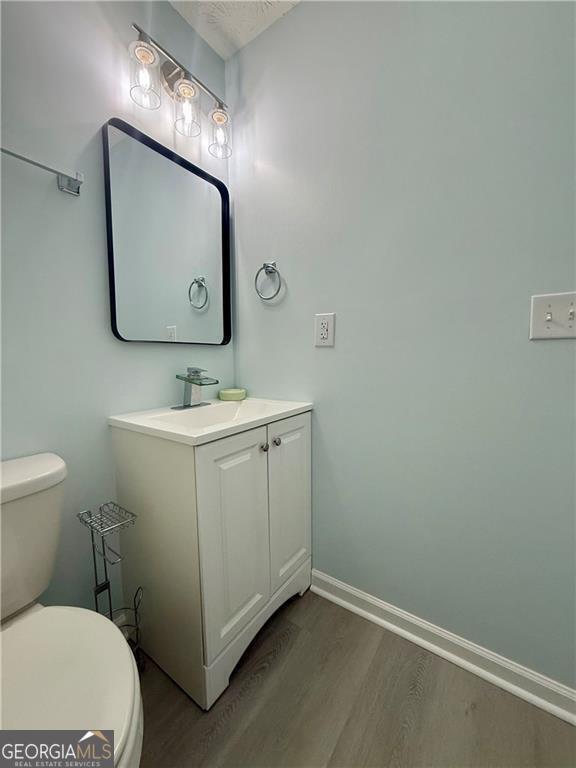 5075 Forest Downs Ln, Atlanta, GA 30349 - half bathroom featuring toilet, baseboards, vanity, and wood finished floors