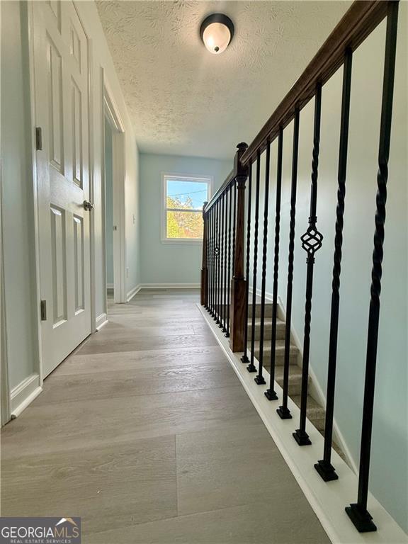 5075 Forest Downs Ln, Atlanta, GA 30349 - hallway featuring a textured ceiling, wood finished floors, baseboards, and stairs