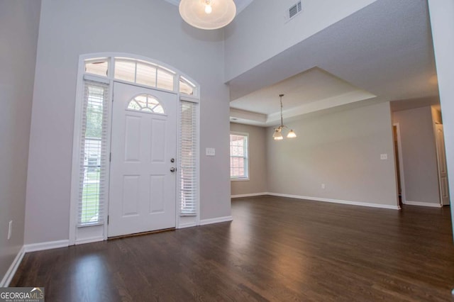 foyer entrance with a raised ceiling, baseboards, visible vents, and wood finished floors