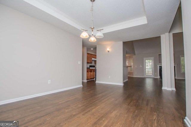 interior space with a notable chandelier, dark wood finished floors, baseboards, a raised ceiling, and ornamental molding