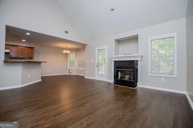 unfurnished living room with baseboards, a notable chandelier, dark wood finished floors, and a tiled fireplace