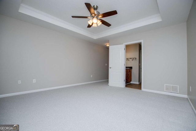 carpeted spare room featuring a raised ceiling, ornamental molding, ceiling fan, and visible vents