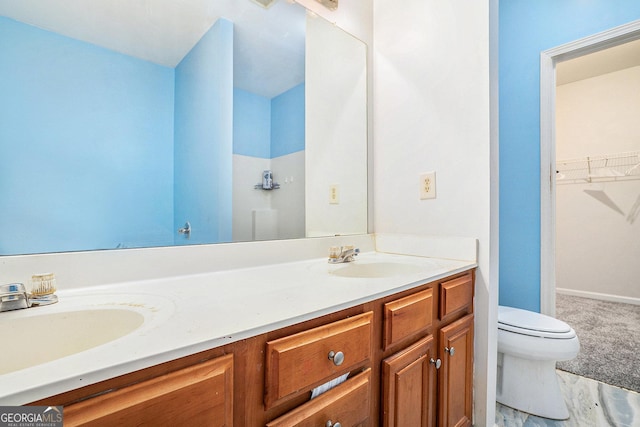 bathroom with toilet, double vanity, and a spacious closet
