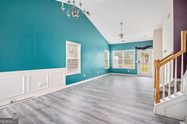 unfurnished living room featuring stairs, a ceiling fan, high vaulted ceiling, wood finished floors, and a chandelier