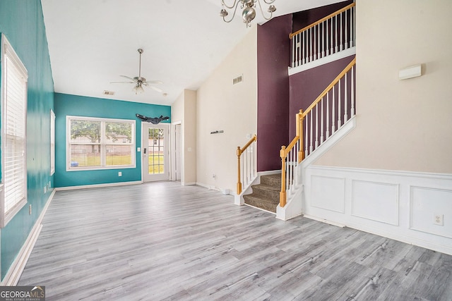 unfurnished living room with wood finished floors, a ceiling fan, stairway, a chandelier, and high vaulted ceiling