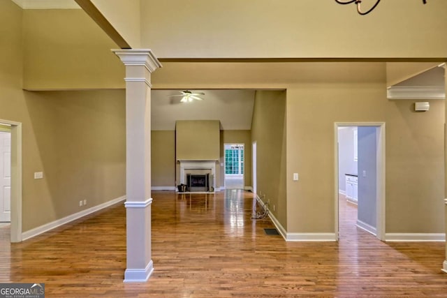 unfurnished living room featuring a ceiling fan, baseboards, wood finished floors, a fireplace, and ornate columns