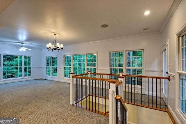 interior space featuring carpet, ornamental molding, a chandelier, a wainscoted wall, and an upstairs landing