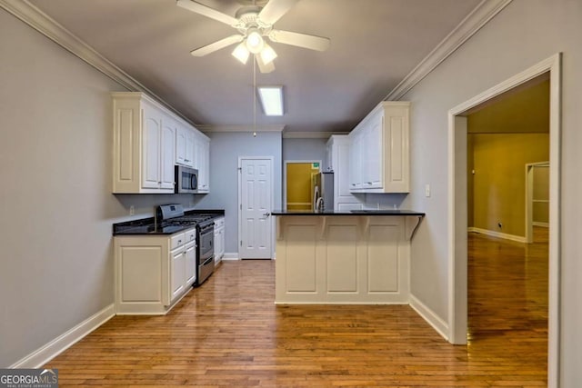 kitchen with ceiling fan, stainless steel appliances, dark countertops, and wood finished floors