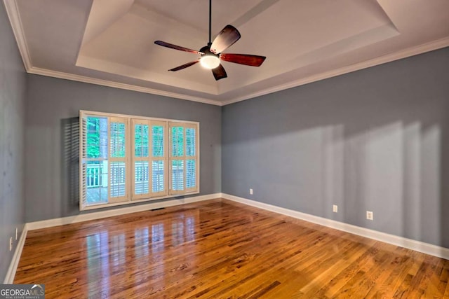 spare room featuring a tray ceiling, baseboards, wood finished floors, and a ceiling fan