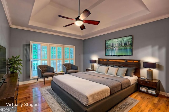 bedroom featuring a ceiling fan, a tray ceiling, baseboards, crown molding, and wood finished floors