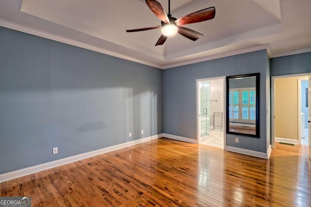 unfurnished room with a tray ceiling, hardwood / wood-style floors, baseboards, ceiling fan, and ornamental molding