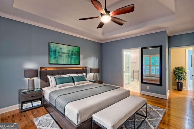 bedroom with a tray ceiling, crown molding, wood finished floors, and baseboards
