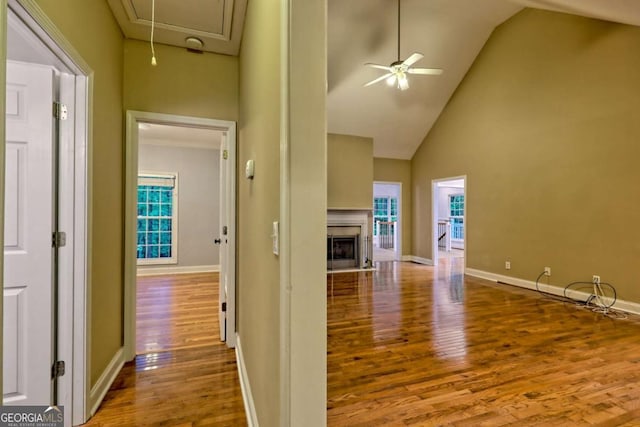hallway with wood finished floors, high vaulted ceiling, attic access, a healthy amount of sunlight, and baseboards