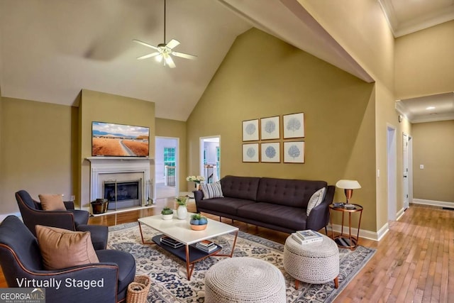 living room with a ceiling fan, high vaulted ceiling, baseboards, a glass covered fireplace, and hardwood / wood-style flooring