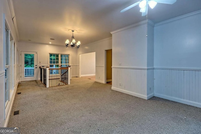 carpeted spare room featuring ornamental molding, ceiling fan with notable chandelier, a wainscoted wall, and visible vents