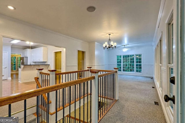 hall with an inviting chandelier, an upstairs landing, a wainscoted wall, a decorative wall, and ornamental molding