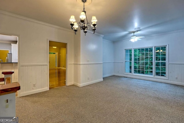 empty room featuring carpet flooring, ornamental molding, a wainscoted wall, and ceiling fan with notable chandelier