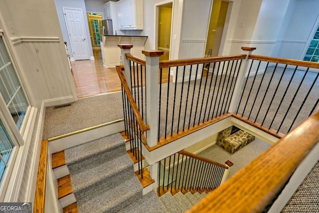 staircase with wainscoting, visible vents, and carpet floors