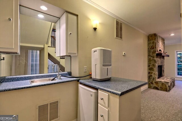 kitchen featuring a sink, ornamental molding, visible vents, a fireplace, and dark countertops