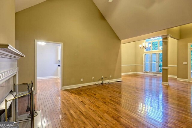 unfurnished living room featuring a premium fireplace, an inviting chandelier, high vaulted ceiling, hardwood / wood-style floors, and ornate columns