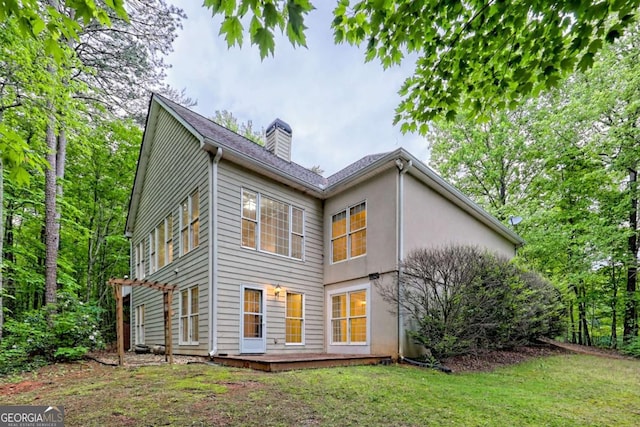 rear view of property with stucco siding, a chimney, and a lawn