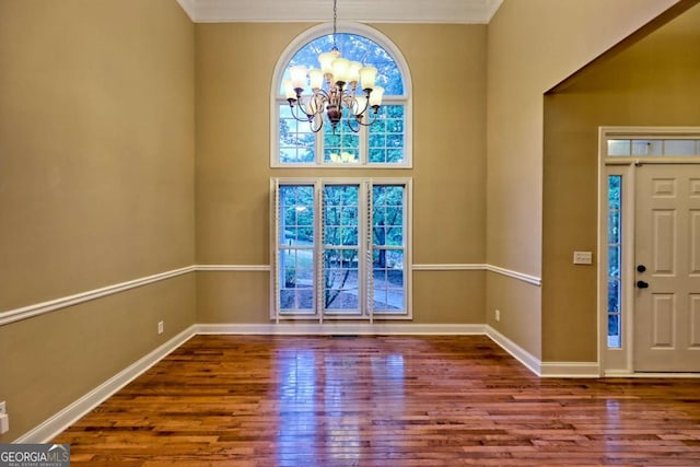 foyer entrance featuring wood finished floors, baseboards, ornamental molding, and a notable chandelier