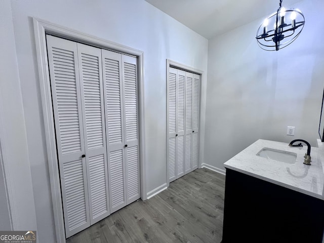 bathroom featuring a closet, wood finished floors, vanity, a chandelier, and baseboards