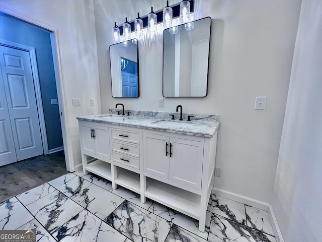 bathroom featuring double vanity, marble finish floor, baseboards, and a sink