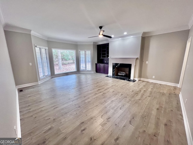unfurnished living room featuring light wood-type flooring, a fireplace, crown molding, ceiling fan, and baseboards