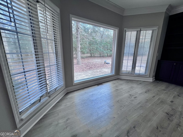 unfurnished dining area featuring baseboards, ornamental molding, visible vents, and wood finished floors