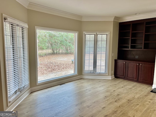 unfurnished dining area with crown molding, light wood-type flooring, visible vents, and baseboards