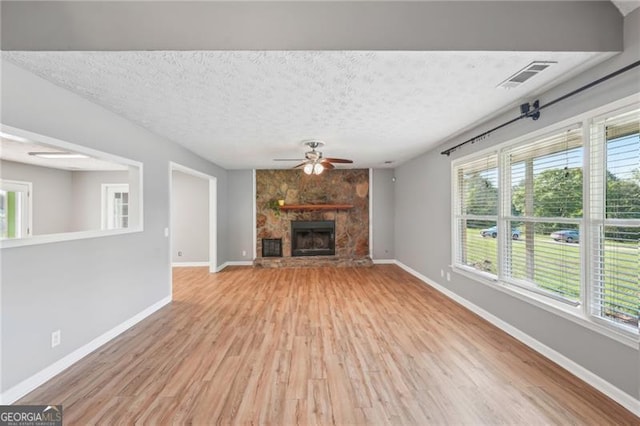 3880 Dial Mill Rd NE, Conyers, GA 30013 - unfurnished living room featuring light wood-style floors, a ceiling fan, baseboards, a stone fireplace, and a textured ceiling