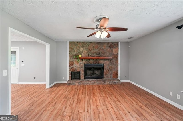 3880 Dial Mill Rd NE, Conyers, GA 30013 - unfurnished living room featuring a ceiling fan, light wood-style floors, a fireplace, baseboards, and a textured ceiling