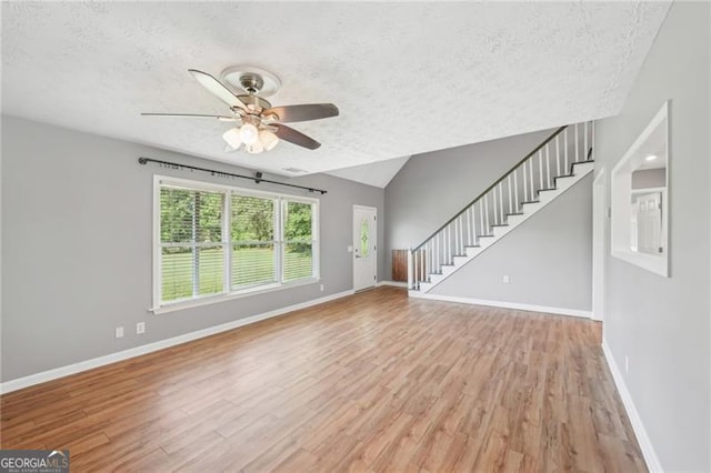 3880 Dial Mill Rd NE, Conyers, GA 30013 - unfurnished living room featuring a textured ceiling, ceiling fan, baseboards, stairway, and light wood-type flooring