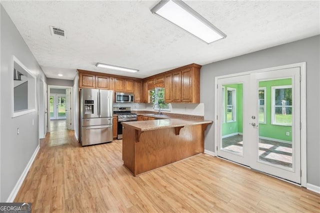 3880 Dial Mill Rd NE, Conyers, GA 30013 - kitchen with appliances with stainless steel finishes, a textured ceiling, a sink, brown cabinets, and light wood-style floors