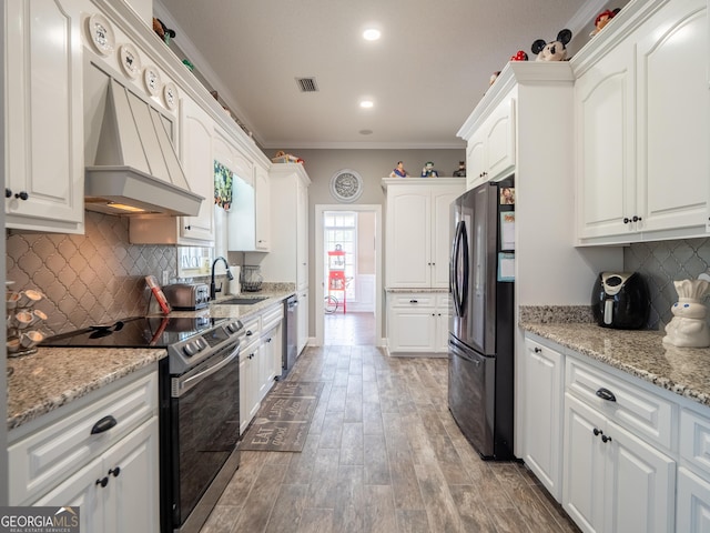 kitchen with ornamental molding, a sink, custom range hood, white cabinets, and appliances with stainless steel finishes
