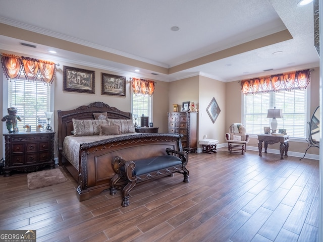 bedroom with wood finished floors, a tray ceiling, visible vents, baseboards, and ornamental molding