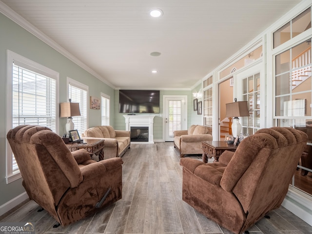 living area featuring baseboards, ornamental molding, a glass covered fireplace, and wood-type flooring