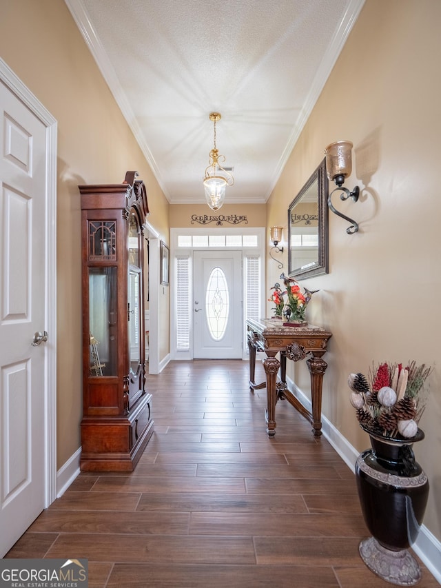 foyer entrance with a chandelier, ornamental molding, baseboards, and dark wood finished floors