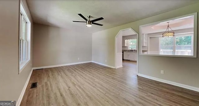 spare room featuring wood finished floors, a ceiling fan, visible vents, baseboards, and arched walkways