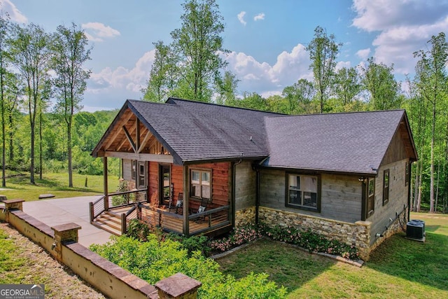 rear view of property featuring a lawn, stone siding, and roof with shingles